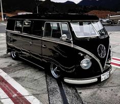 an old black vw bus parked in a parking lot with mountains in the background