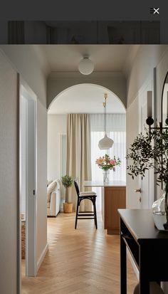 an archway leading into a living room and dining area with wood floors, white walls and curtains