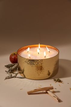 a candle that is sitting on a table next to some sticks and an apple in front of it