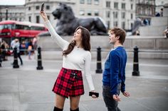 a man and woman standing next to each other in front of a statue holding up their cell phones