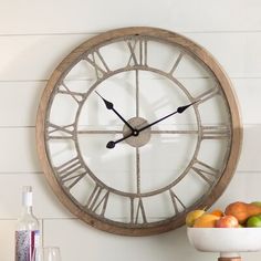 a large clock mounted to the side of a wall next to a bowl of fruit