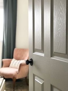 an open door leading to a living room with a chair and window in the background