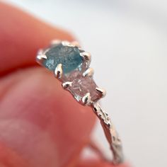 a close up of a person's hand holding an engagement ring with two stones