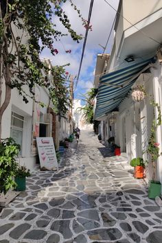 an alley way with white buildings and trees on both sides, surrounded by cobblestones