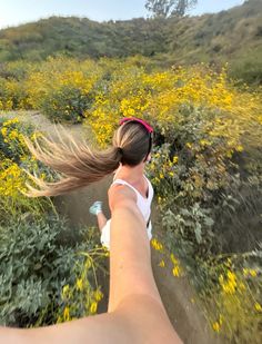 a woman is running down a trail with her hair blowing in the wind and yellow wildflowers behind her