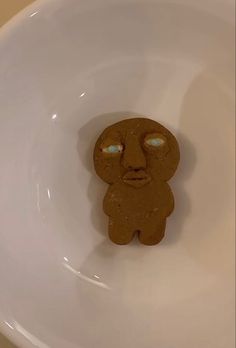 a cookie shaped like a man with eyes wide open sitting in a white bowl on the counter