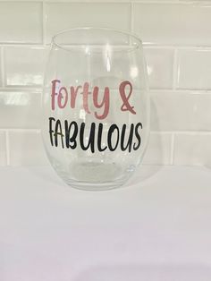 a wine glass with the words forty and fabulous written in black ink on it sitting on a counter