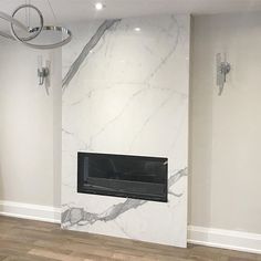 an empty room with a fireplace in the middle and white marble on the back wall