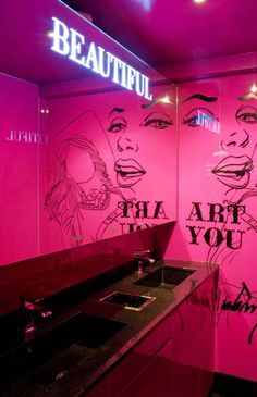 a bathroom with pink walls and graffiti on the wall, along with black counter tops