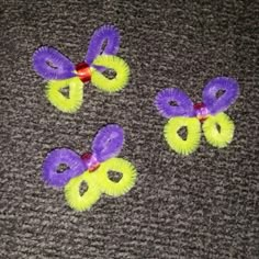 three purple and yellow hair clips on a gray carpeted floor with red ribbon around them