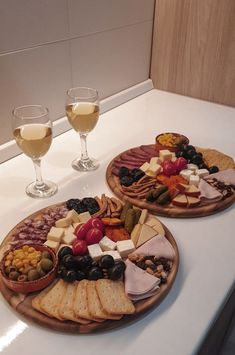 two wooden plates filled with cheese and crackers next to wine glasses on a counter