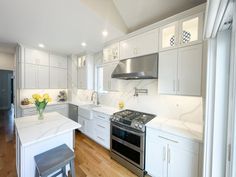 a kitchen with white cabinets and stainless steel stove top oven, counter tops, and stools