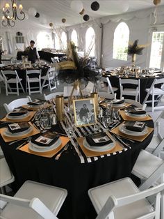 a black and gold table setting for an event with white chairs, silver napkins and plates