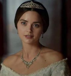 a woman wearing a tiara and necklace in a white dress with gold trimmings