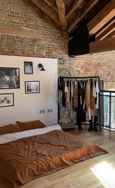 a bed in a bedroom next to a brick wall with clothes hanging on the rails