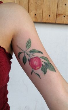 a woman's arm with an apple and leaves tattoo on the left side of her arm