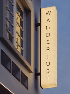 a white sign hanging from the side of a building next to a window with shutters