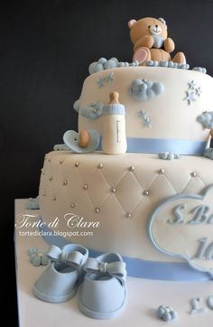 a three tiered cake with baby shoes and a teddy bear on top