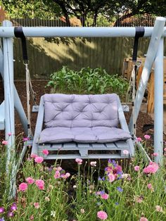 a swing bed is in the middle of some flowers and plants, with purple cushions on it