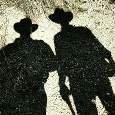 two people standing next to each other with hats on their heads and shadows in the dirt