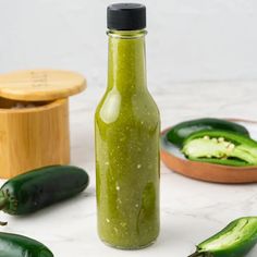 a bottle filled with green stuff next to other vegetables on a table and in bowls