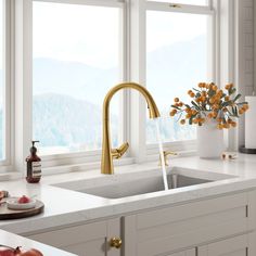 a kitchen sink with a gold faucet and orange flowers in the window sill