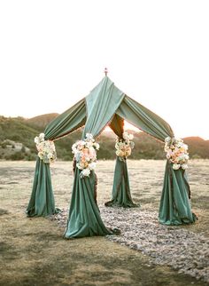 an outdoor wedding setup with green draping and flowers on the side of it