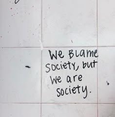 a white tiled wall with graffiti written on it and the words we blame society but we are society