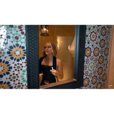 a woman standing in front of a mirror holding a drink and looking into the bathroom