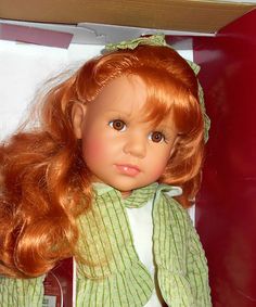 a red haired doll in a box with her hair pulled back and wearing a green scarf