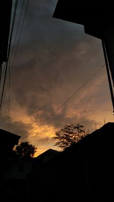 the sun is setting over some houses and power lines in the distance, with trees silhouetted against the sky