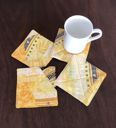 four yellow coasters and a white cup on a wooden table with a brown surface