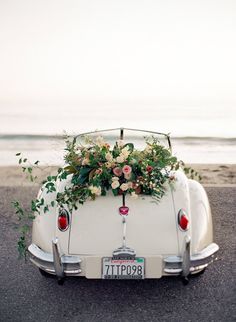 an old car with flowers and greenery on the hood parked in front of the ocean