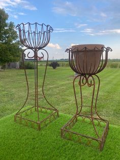 two metal planters sitting on top of a lush green field