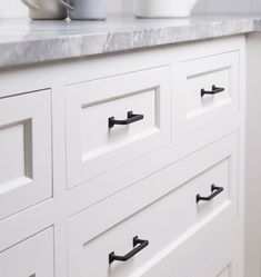 a white cabinet with black handles and knobs on it's doors is seen in this image