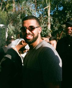 a man wearing sunglasses standing in front of a group of people with trees behind him