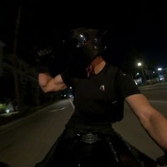 a man riding on the back of a motorcycle down a street at night wearing a helmet