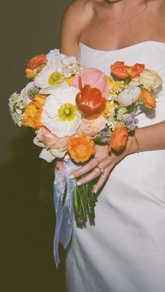 a woman in a white dress holding a bouquet of orange and white flowers on her wedding day