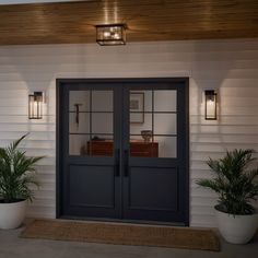 two potted plants sit on the side of a white house with black doors and windows