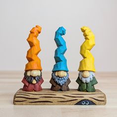 three colorful gnomes sitting on top of a piece of wood