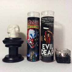 two halloween candles and a candle holder on a white surface with a skull in the middle