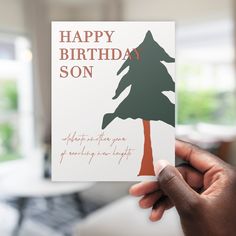 a person holding up a card with a tree on it that says happy birthday son