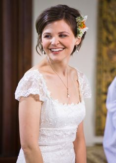 a woman in a white dress smiles at the camera while wearing a flower in her hair