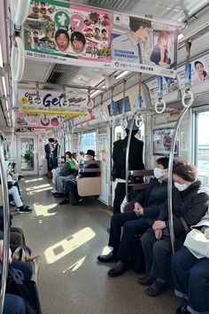 people wearing masks are sitting on the subway car, with posters above them and hanging from the ceiling