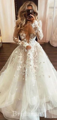 a woman taking a selfie in a wedding dress with flowers on the skirt and long sleeves