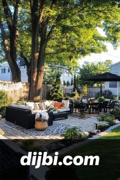 an outdoor living area with couches, tables and chairs under a large tree in the back yard