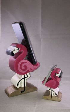 a pink flamingo holding a cell phone in it's beak and standing on its legs