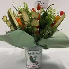 a bucket filled with vegetables sitting on top of a white tablecloth covered table next to a sign