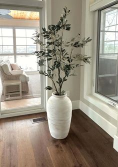 a white vase filled with flowers sitting on top of a wooden floor next to a window