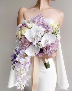 a woman wearing a white dress holding a bouquet of purple and white flowers in her hands